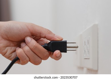 Men's hands are Plug in power outlet adapter cord charger of laptop computer On wooden floor With sun Warm light