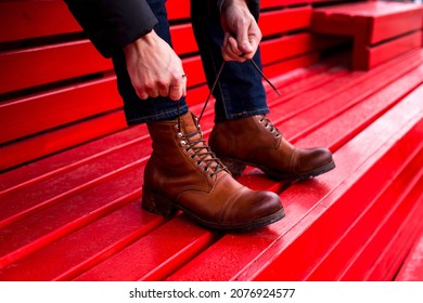 Men's hands tie their shoelaces on leather brown shoes on a red wooden background. Beautiful photo of men's stylish handmade shoes