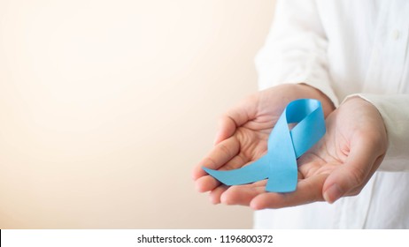 Men's health and prostate cancer awareness campaign in November month. Close up of young man hands holding light blue ribbon awareness. Symbol for support men who living w/ cancer. Copy space.