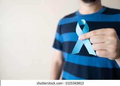 Men's health and Prostate cancer awareness campaign in November month. Close up of young man hands holding light blue ribbon awareness. Symbol for support men who living with cancer. Copy space.