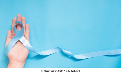 Men's health and Prostate cancer awareness campaign concept. Man hands holding light blue ribbon awareness w/ long tail on sky blue background. Symbol for support men who living w/ cancer. Copy space.