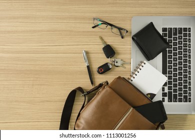 Men's leather bag with personal items and laptop on wood desk.