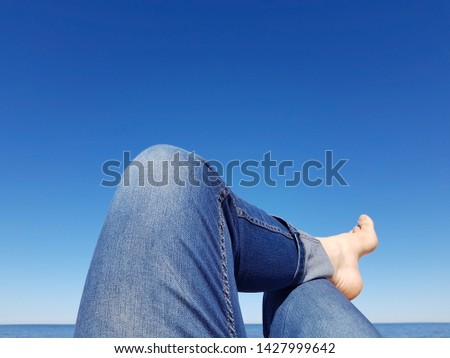 Men's legs in blue jeans against a beautiful blue sky and water. Beach-themed