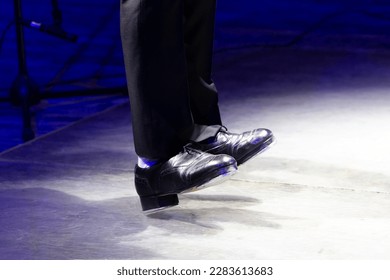 Men's legs in motion in stage trousers with stripes and leather shoes for Irish dancing on the floor. Black work boots for tap dancing with reflection on floor. selective focus. Step on stage close-up - Powered by Shutterstock