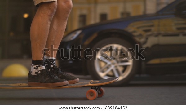 Men\'s legs on a skateboard move on the road\
towards cars. The legs of a light-skinned European man on a\
longboard rides on the highway. Close\
Up.