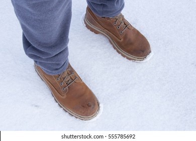 Men's Legs In Work Shoes And Gray Sweatpants, Snow Background, Side Perspective