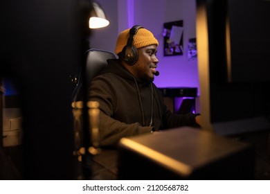 Men's Room Darkly Lit With Purple Led Lights, A Portrait From Behind A Monitor Of A Man Of American Descent Wearing A Yellow Cap With A Headset. The Guy Is Playing Shooting Games On A Computer.