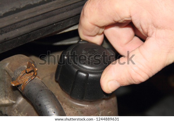 Men\'s rough hand unscrews the cap of the\
expansion tank, checks the coolant antifreeze on the old car -\
vehicle maintenance