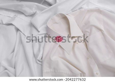 Men's shirt with lipstick kiss mark among other clothes as background