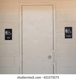 A Men's And Women's Bathroom Sign In Black On A Cinder Block Wall