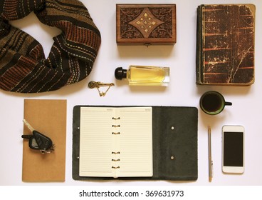 Men's Or Women's Different Accessories: Brown Scarf, Golden Brooch, Perfume, White Cellphone, Empty Notepad, Pen, Car Keys, Vintage Book, Wooden Box On White Background