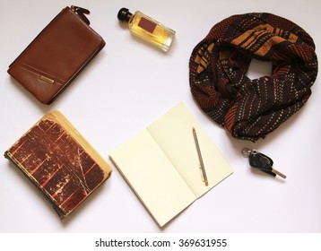 Men's Or Women's Different Vintage Accessories: Brown Scarf, Handbag, Perfume, Empty Sketchbook, Pen, Car Keys, Old Book On White Clear Background Top View