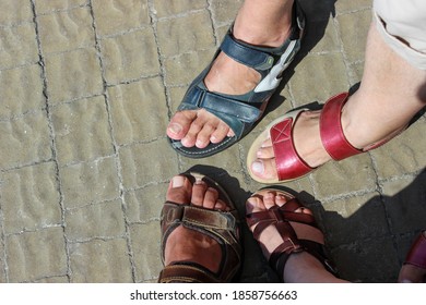 Men's and women's feet shoes in sandals, on a stone pavement in the sunlight
