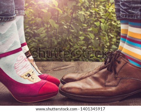 Men's and women's legs in fashionable shoes, bright, multi-colored socks on a wooden terrace on the background of green trees and sunlight. Close-up. Concept of Style, Fashion and Beauty