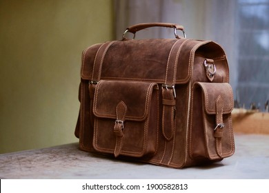 Men's work bag made of cowhide. Photo created in a bag workshop. In the background are bag work tools. Briefcase made of brown leather. Satchel to work. Retro leather bag for men. 