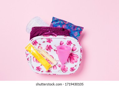 Menstrual cup, tampon and pad in a toiletry bag on a pink background. Concept of critical days, menstruation. Female intimate hygiene period products, top view