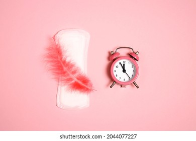 Menstrual Pad With Feather And  Alarm Clock On Pink Background. Menstruation Cycle Period, Woman Hygiene.