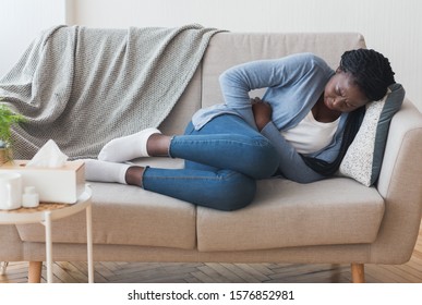 Menstrual Pain. Sick Young Black Woman Lying On Couch At Home Suffering From Abdominal Ache