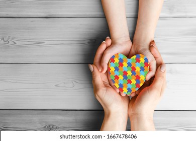 Mental Health Care Concept With Puzzle Or Jigsaw Pattern On Heart Female Hands Hold Childrens Palms With A Red Heart In Them. The Concept Of Family Love And Support. World Autism Awareness Day