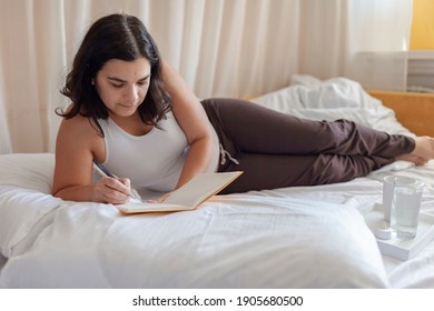 Mental Health Care, Positive Thinking And Wellness Concept. Attractive Woman Lying In Bed, Practicing Stress Relief Challenge With Journal About Feeling, Glass Of Water And Gratitude List