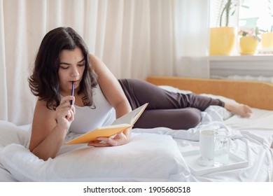 Mental Health Care, Positive Thinking And Wellness Concept. Attractive Woman Lying In Bed, Practicing Stress Relief Challenge With Journal About Feeling, Glass Of Water And Gratitude List