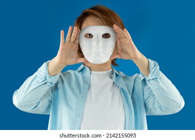 Mental Health Concept. Young Man Holding A Full-face Mask, Ball, Or Masquerade Carnival Mask. Symbol Of Bipolar Disorder Or Hypocrisy, Deceit, Duplicity. Portrait Of Guy Prep Student With Long Hair 