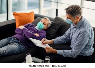 Mental Health Professional Taking Notes During A Session With His Patient. They Are Wearing Protective Face Masks Due To Coronavirus Pandemic. 