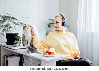 Mental Health And Work. Work Life Balance. Young Woman In Headphones Near Laptop At Home Office Resting After Work. Freelancer Woman Play With Cat And Eating Health Food, Taking Break Time