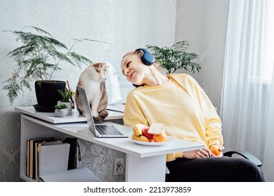 Mental Health And Work. Work Life Balance. Young Woman In Headphones Near Laptop At Home Office Resting After Work. Freelancer Woman Play With Cat And Eating Health Food, Taking Break Time