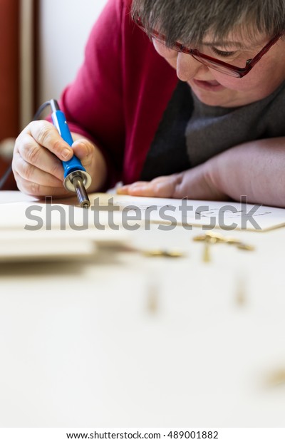mentally disabled woman is doing\
woodburning with burning pen as art therapy,\
vertical