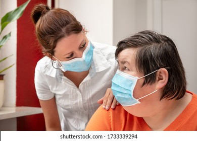 Mentally Disabled Woman And Nurse Or Caretaker Wearing A Surgical Mask, Covid-19 Or Corona, Coronavirus And Handicapped People