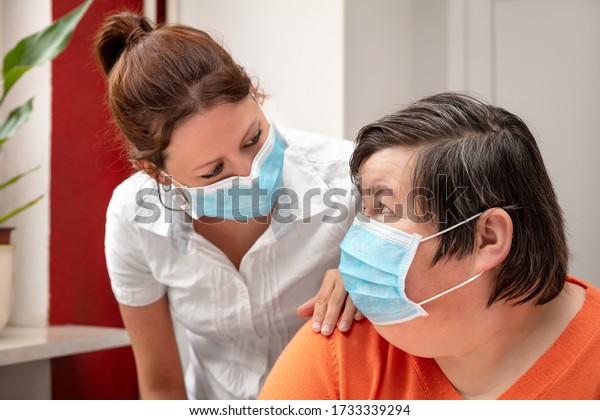 Mentally disabled woman and nurse or caretaker\
wearing a surgical mask, covid-19 or corona, coronavirus and\
handicapped people