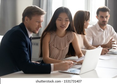Mentor coach helping Asian female employee with corporate software, diverse colleagues working on project together at group meeting, discussing statistics, using laptop, manager consulting client - Shutterstock ID 1531731407