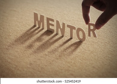MENTOR wood word on compressed board with human's finger at R letter