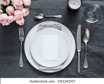 Menu, wedding invitation mock up. Beautiful table setting on gray linen tablecloth. Festive table setting for wedding dinner with pink spray roses and cabdle. Holiday dinner, white plates. Copy space