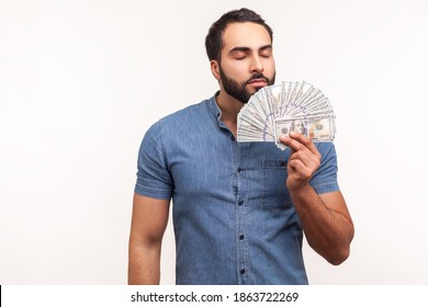 Mercantile bearded man enjoying smell of hundred dollar bills he holding, first big salary, reward for business idea. Indoor studio shot isolated on white background