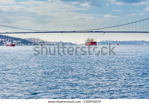 Merchant ship\
passing through Bosphorus  Bridge with background of Bosphorus\
strait on a sunny day with background cloudy blue sky and blue sea\
in Istanbul, Turkey. Blue Turkey\
concept.
