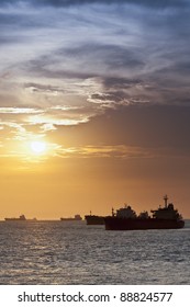 Merchant Ships In Silhouette Backlit By The Sun Set