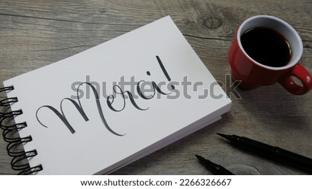 MERCI! lettering in notebook with cup of coffee and pens (THANKS! in French)