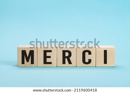 Merci - Thank you in French language. Merci Word on Letter Tiles on blue Background. Minimal aesthetics. Word merci thank you in french on wooden cubes
