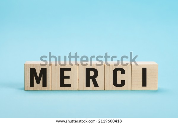 Merci - Thank you in French language. Merci\
Word on Letter Tiles on blue Background. Minimal aesthetics. Word\
merci thank you in french on wooden\
cubes