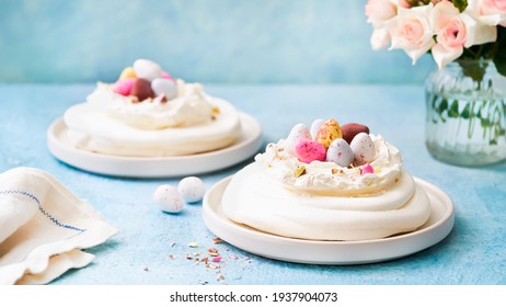 Meringue Nest Cake With Colorful Chocolate Eggs, Buttercream Frosting On Light Blue Background Banner With Copy Space. Selective Focus. Food Idea For Kids. Easter Cake. Close Up. Spring Feast Concept.