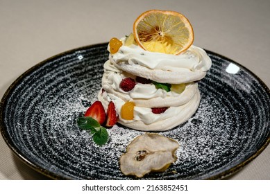 Meringue Pavlova dessert cake with fresh berries on a black plate. Pavlova white dessert with fresh fruits. Sweet meringue delicious dessert close up view