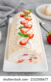 Meringue roll Pavlova cake with cream and fresh strawberries on top on a gray background. Copy space.