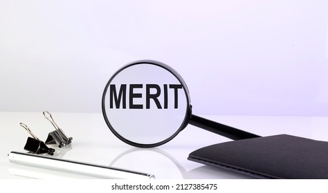 MERIT Concept. Magnifier Glass Text With Notebook And Pen