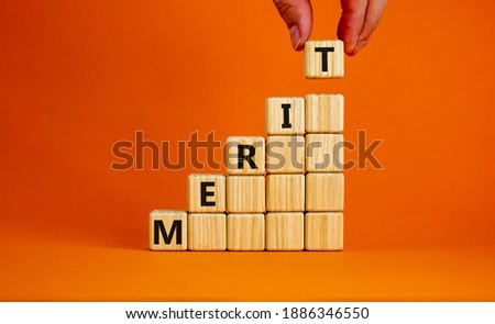 Merit symbol. Wood cubes with word 'merit' stacking as step stair on beautiful orange background, copy space. Male hand. Business and merit concept.