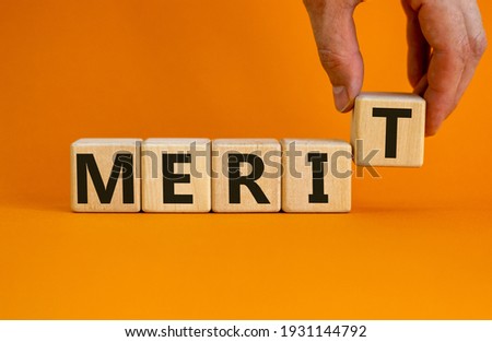 Merit symbol. Wooden cubes with the word 'merit'. Businessman hand. Beautiful orange background, copy space. Business and merit concept.
