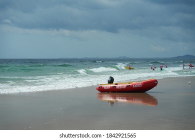 Mermaid Beach QLD Australia 10/25/2020: Surf Life Saving Water Craft Parked On The Shore Ready For A Rescue With A Group Of Little Nippers Board Training In The Background On A Stormy Day.