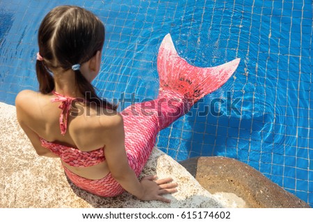Mermaid girl with pink tail on rock at poolside put feet in water. Top view. Fun, vacation concept. Text space