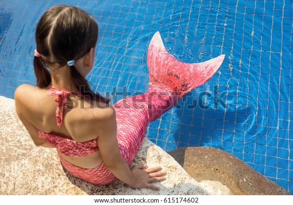 Mermaid girl with\
pink tail on rock at poolside put feet in water. Top view. Fun,\
vacation concept. Text\
space